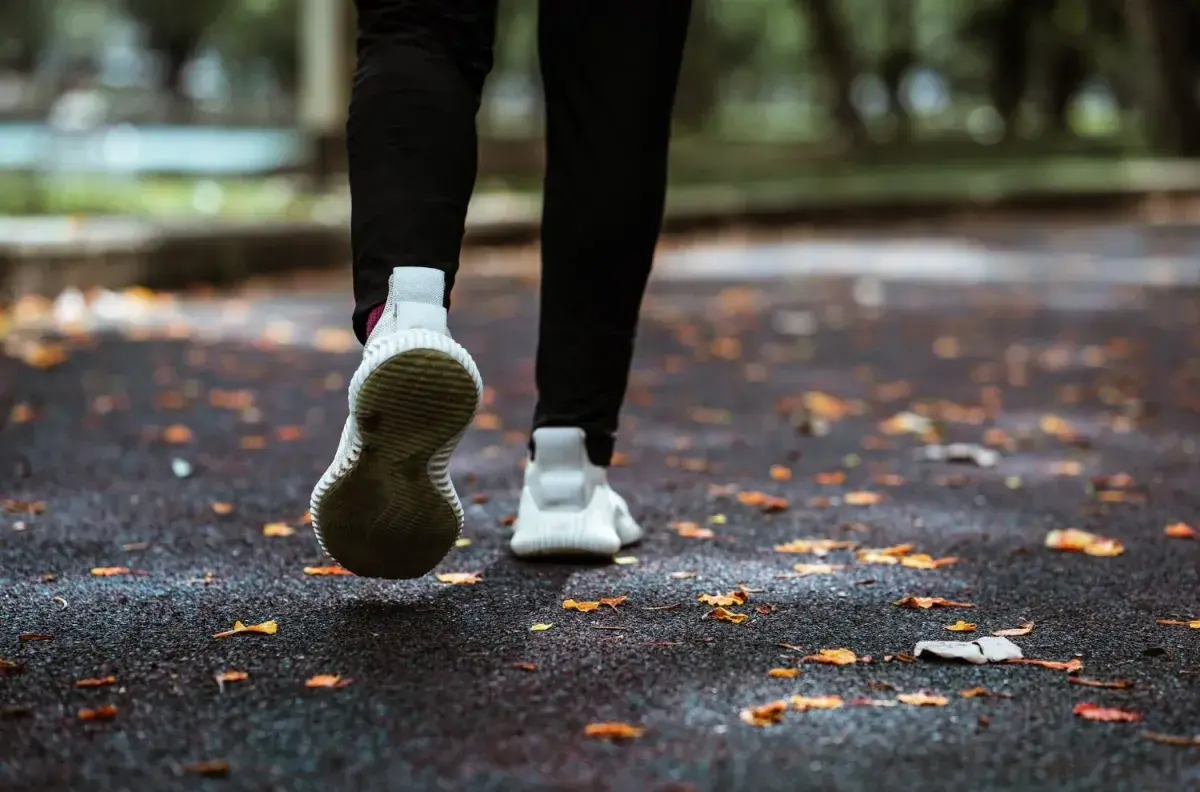 Close-up of a runner's shoes on a leaf-strewn path