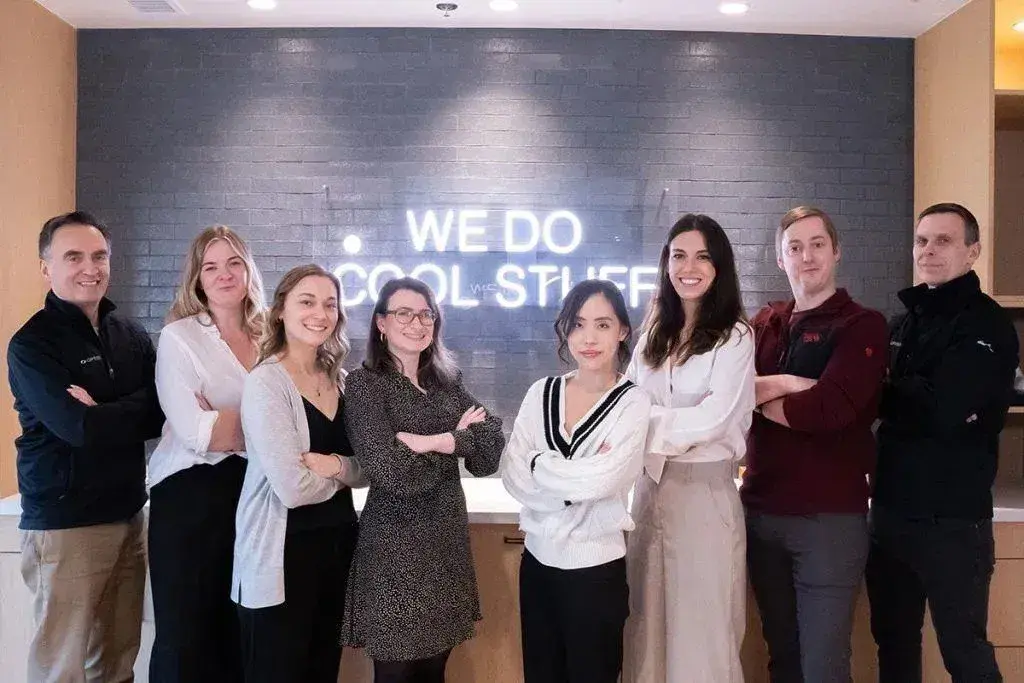 The Optispan team gathered in the office under a neon sign reading “We do cool stuff”