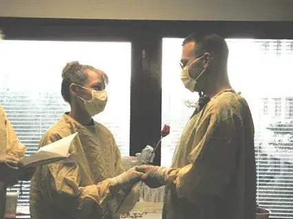 Matt Kaeberlein and Tammi holding hands during their ceremony, both in gowns and face masks